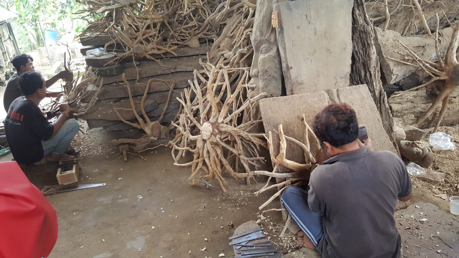 Mehrere Handwerker schnitzen kunstvolle Skulpturen aus verschlungenen Baumwurzeln in einer offenen Werkstatt.