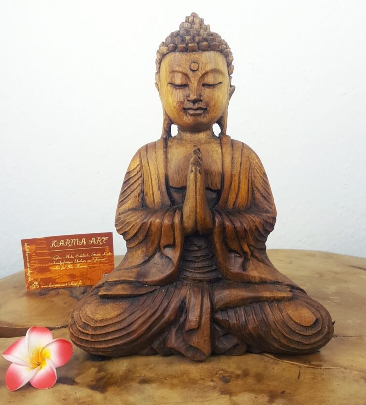 Holzstatue eines sitzenden Buddha mit geschlossenen Augen und gefalteten Händen in Gebetshaltung auf einem Holztisch.